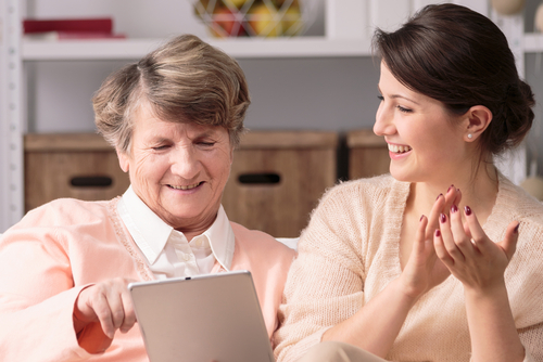 female caregiver teaching elderly woman tablet